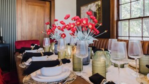 A dining table set with white plates, gold and green glassware, and red flowers in a vase. - Hoosier Memories! Luxury Stay, Steps from IU - Pool Table, Firepit & More (Bloomington)