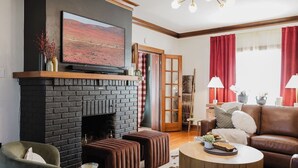 A cozy living room with a black brick fireplace, a leather sofa, a round coffee table, and a mounted painting. - Hoosier Memories! Luxury Stay, Steps from IU - Pool Table, Firepit & More (Bloomington)