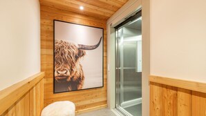 A hallway with wooden paneling, a framed picture of a yak, and a glass elevator door. - Chalet La Vue (Les Crettaux - Nendaz) (Isérables)