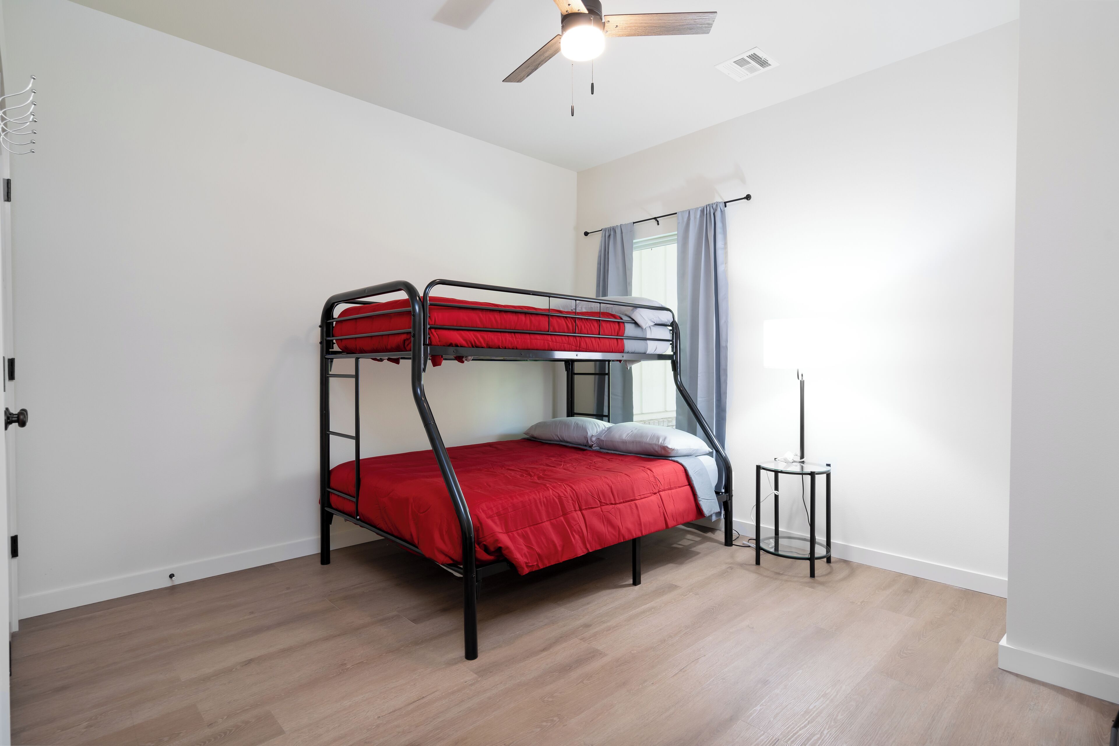 A bunk bed with red bedding in a room with wooden flooring and a ceiling fan.