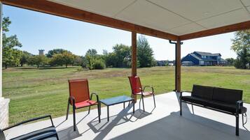 An outdoor patio with a covered seating area, a grassy lawn, and a distant view of a house.