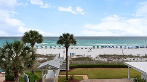 A beach view with palm trees, a covered walkway, and beach umbrellas.