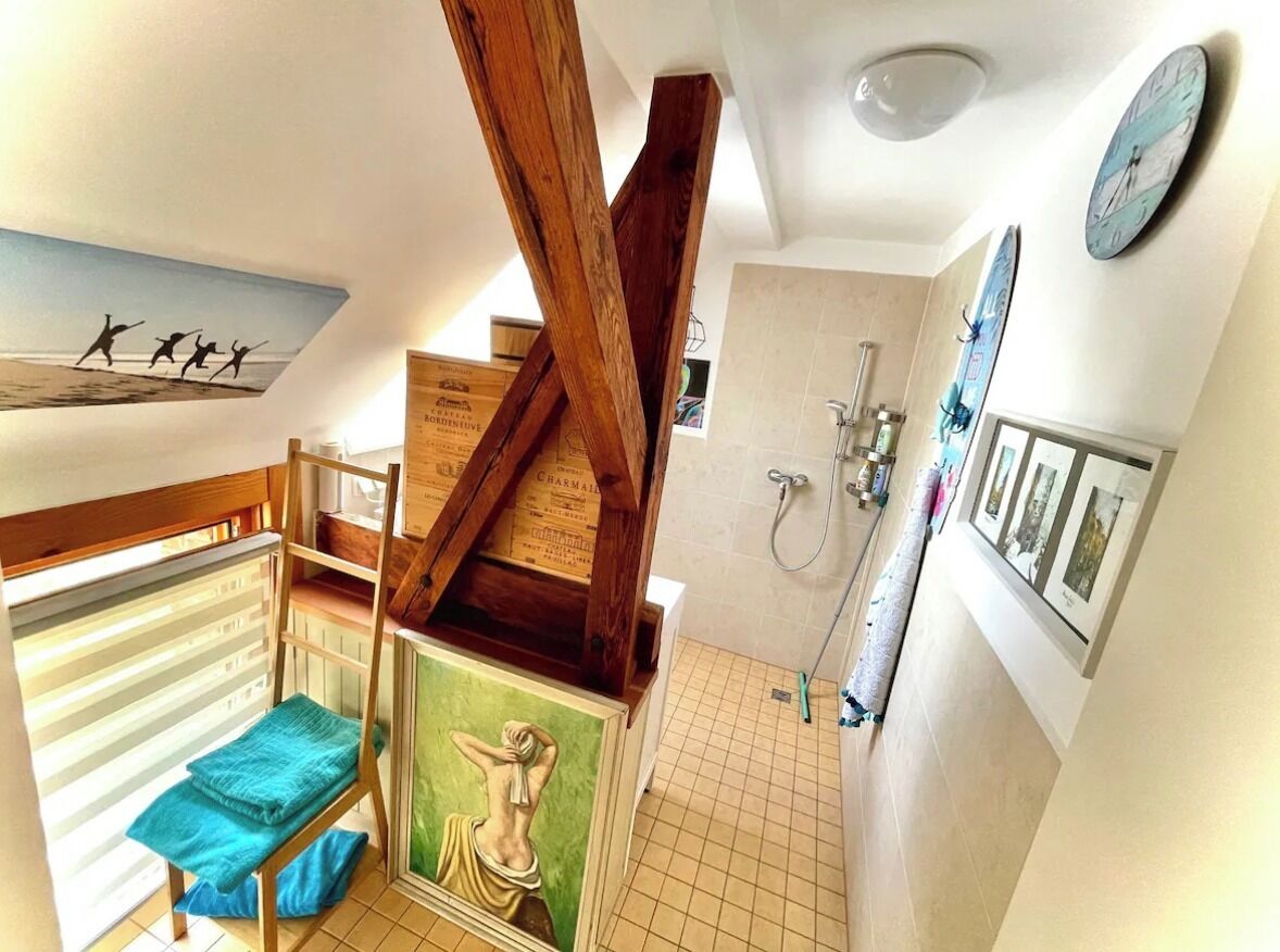 A room with a bunk bed, a wooden ceiling beam, a shower area, and a wall with framed pictures.