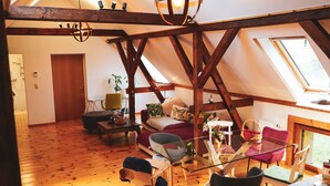 Camera mansarda accogliente con travi a vista in legno, un lucernario, un divano, un tavolo da pranzo e un angolo cottura.