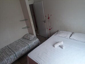 A bedroom with a single bed and a smaller bed, both with white linens. There is a red plant in the corner and a glass shelf on the wall. - Lar Jampa - Acomodações  (João Pessoa)