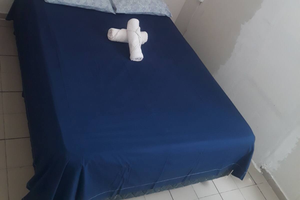 Ein schlichter, kleiner Raum mit einem Bett, Kissen und einem weißen Handtuch.