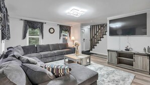 A modern living room with a grey sectional sofa, a coffee table, and a TV mounted on the wall.