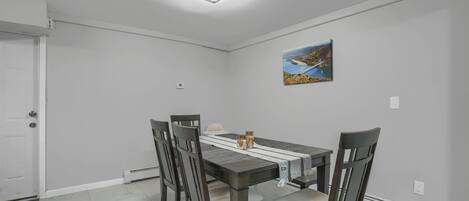 A dining room with a rectangular table, four chairs, a white door, a ceiling light, and a framed picture on the wall.
