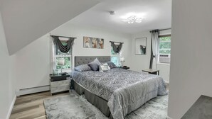 A modern bedroom with a large bed, a nightstand, a dresser, and a window with curtains.