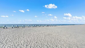 A wide sandy beach with rows of blue and white beach umbrellas and lounge chairs. - Seaside Beach & Racquet Club 5214 (Orange Beach)