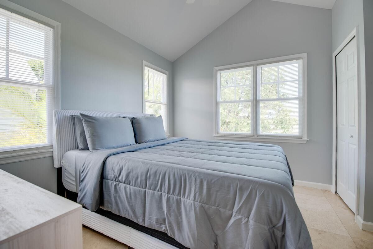 A bedroom with a bed, two windows, a door, and a small table.