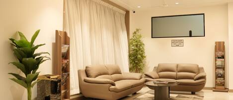 Una sala de estar moderna con dos sofás beige, una mesa de centro y un televisor de pantalla plana grande montado en la pared.