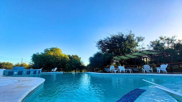 Une piscine à l’eau d’un bleu cristallin, entourée de chaises et de tables en plastique blanc, le tout abrité sous une pergola.