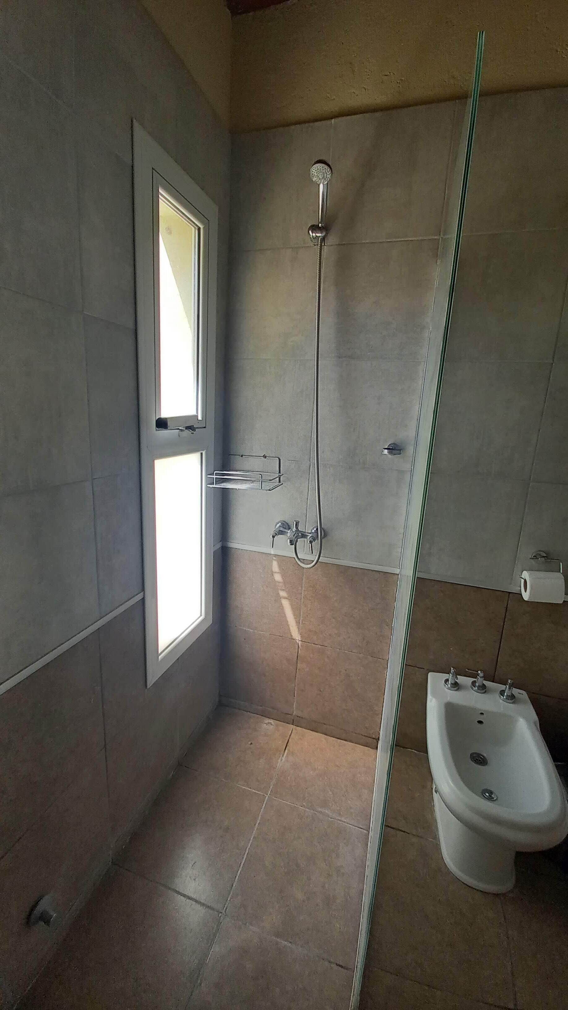 A bathroom with a shower, toilet, and a window.