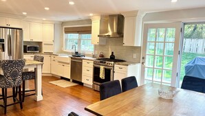 A modern kitchen with white cabinetry, stainless steel appliances, and a dining area with a wooden table and chairs. - Spacious 5bdrm home- saltwater pool, WiFi, AC, private beach parking pass (Westerly)