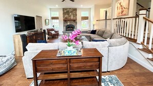 A spacious living room with a stone fireplace, a large sectional sofa, a wooden coffee table, and a television. - Spacious 5bdrm home- saltwater pool, WiFi, AC, private beach parking pass (Westerly)