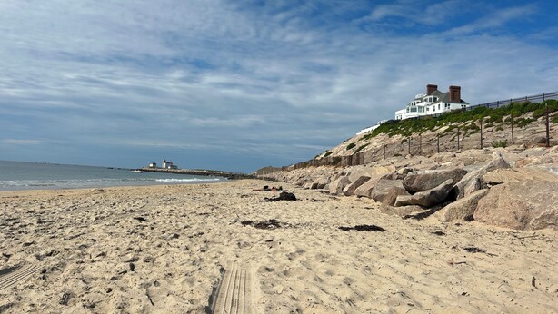 A sandy beach with a white building on a rocky hill, a lighthouse in the distance, and a clear sky. - Spacious 5bdrm home- saltwater pool, WiFi, AC, private beach parking pass (Westerly)