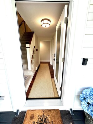 A hallway leading to a staircase with a doormat and a door with a security device.