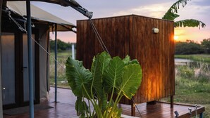 A wooden structure with a concrete planter containing large leafy plants, a metal pole, and a wooden deck. - The Alampara resort (Cheyyur)