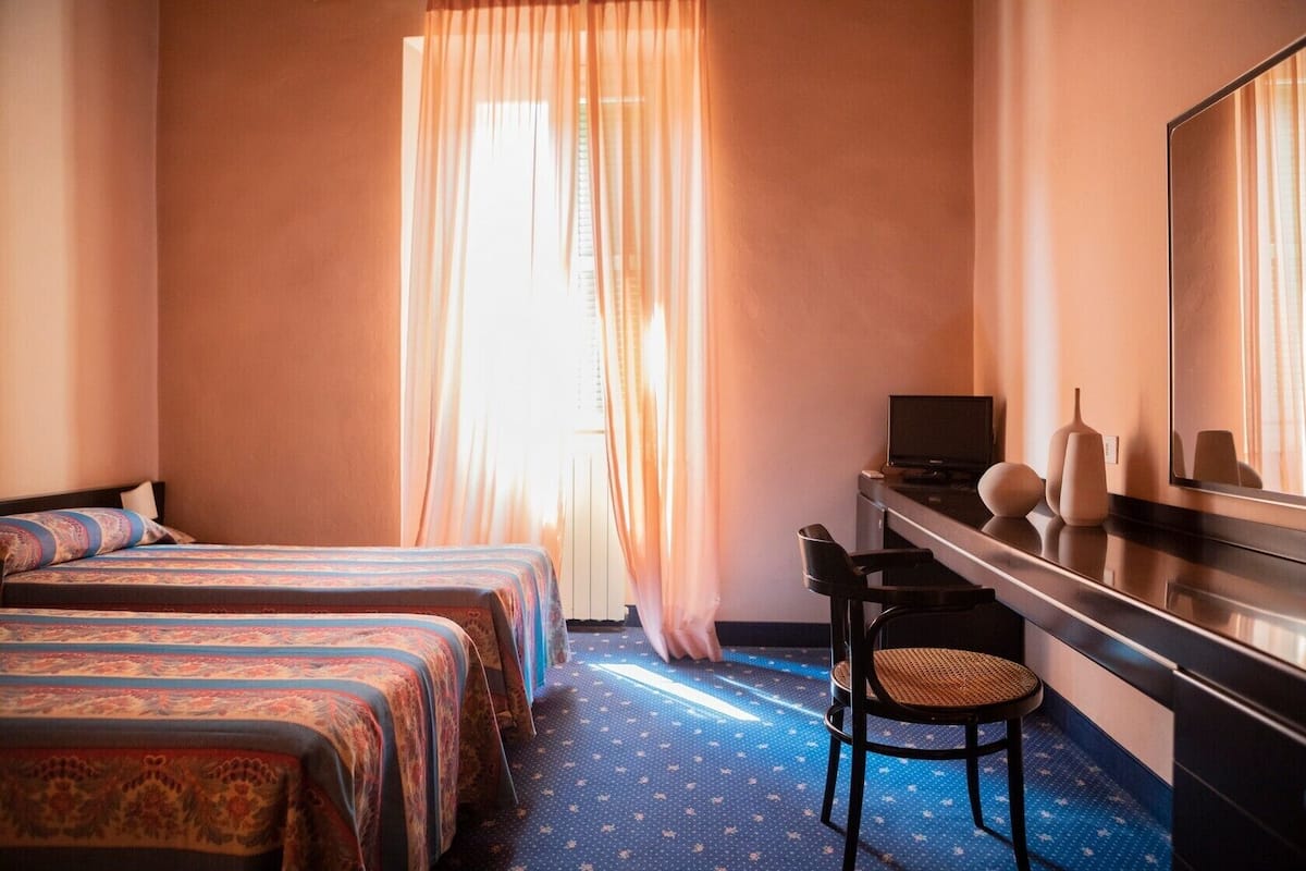 A hotel room with two beds, a desk with a computer, a chair, and a large mirror.