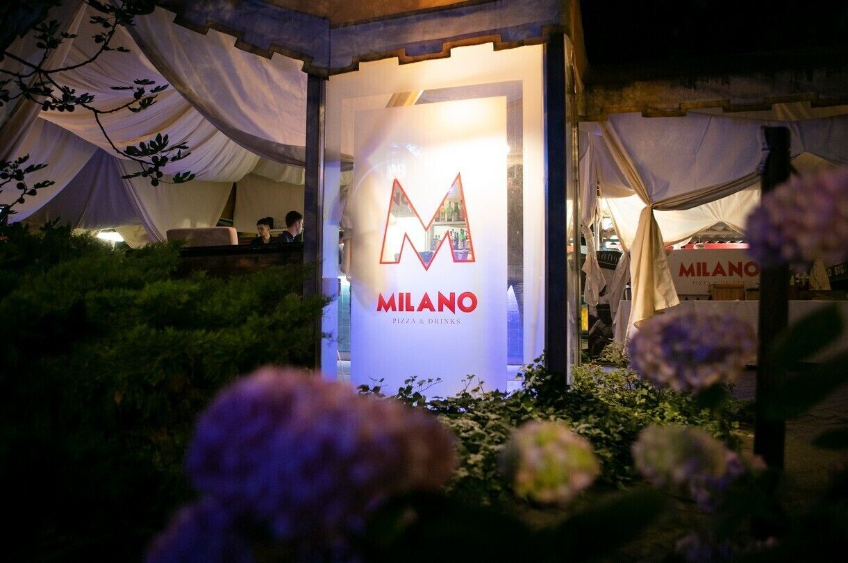 A tented outdoor area with a sign for 'MILANO PIZZA & DRINKS'.