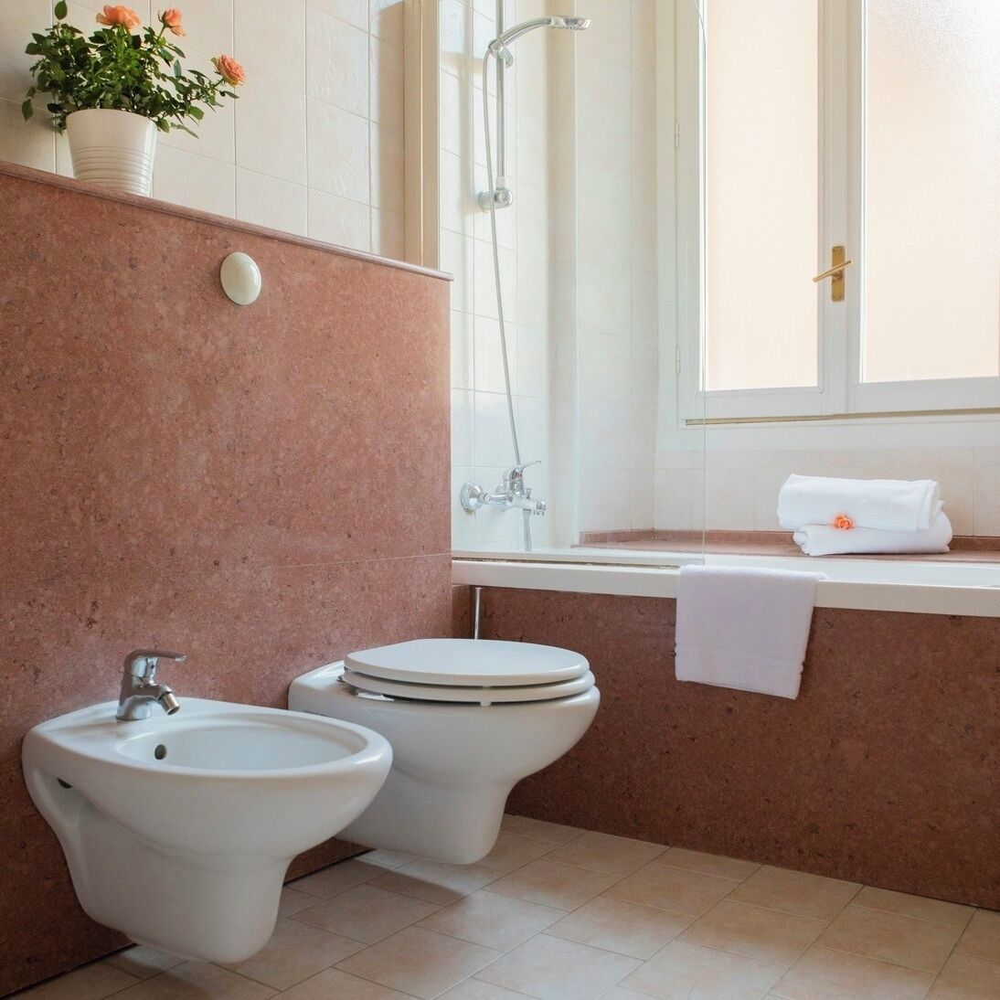 Un bany amb bidet, vàter i rentapèns. Hi ha una finestra amb una tovallola al davantell.