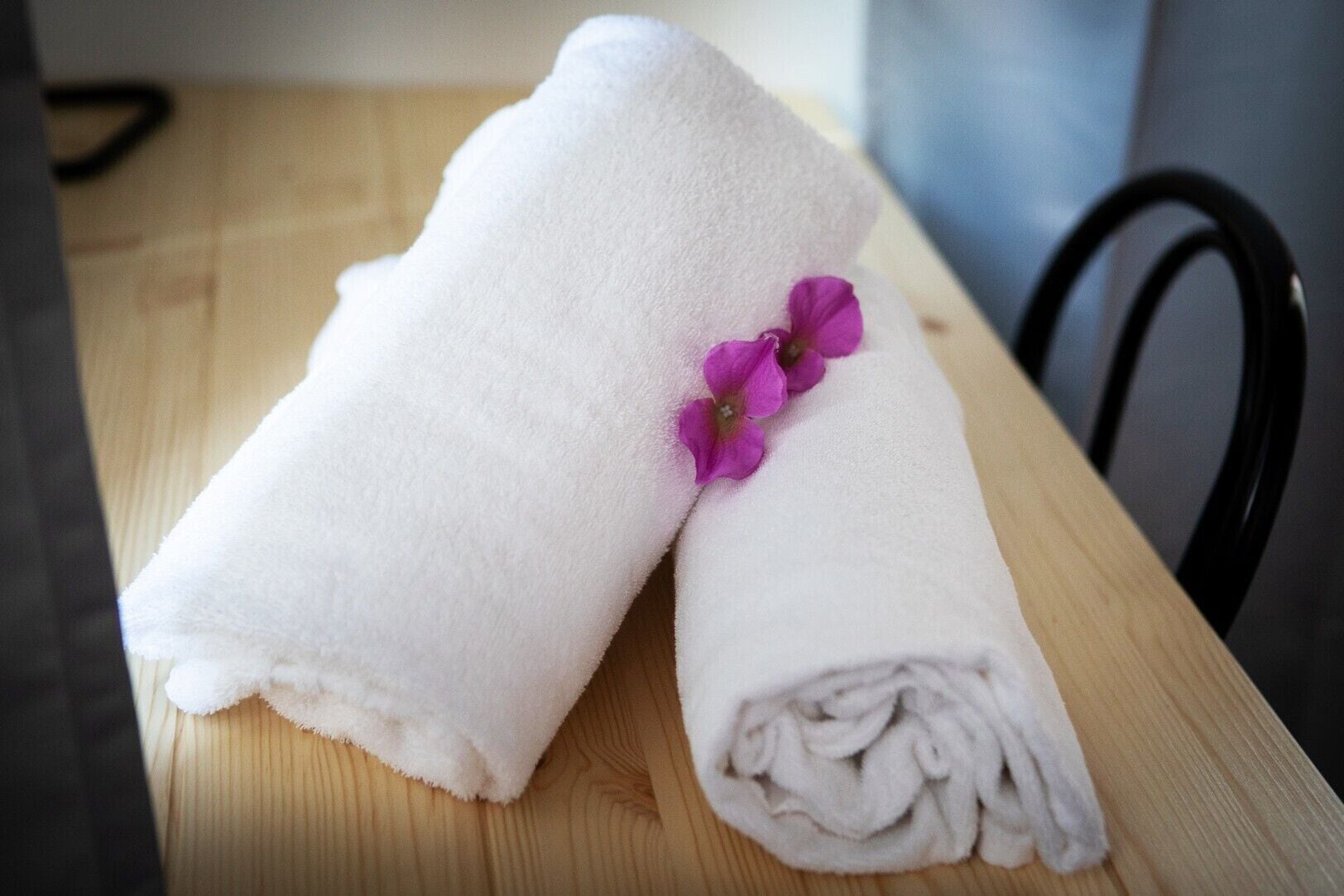 Two white towels with a purple flower on a wooden table.