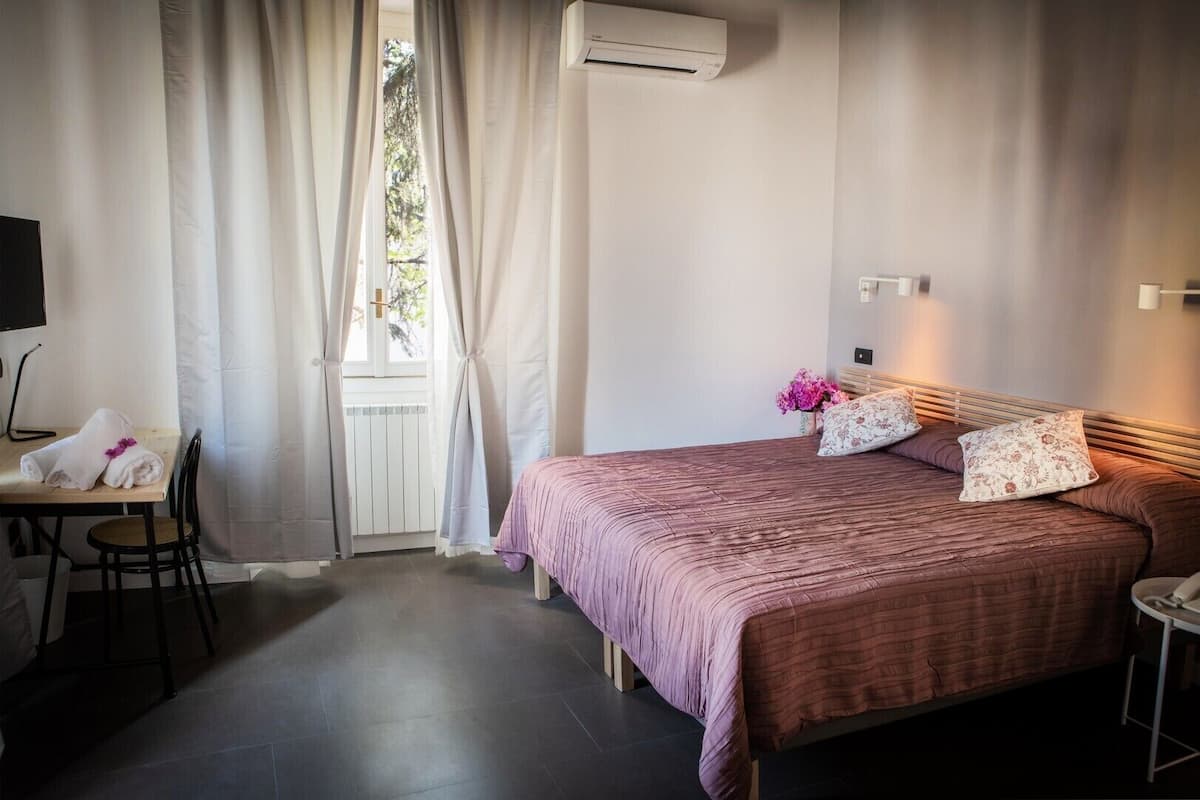 A bedroom with a bed, a desk, and a window with curtains.