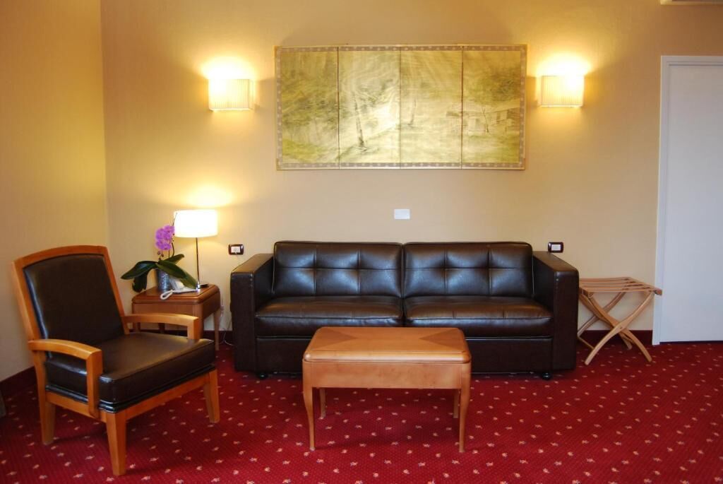 Una sala de estar con un sofá de cuero, un sillón de madera, una pequeña mesa de madera y una alfombra roja con diseño.