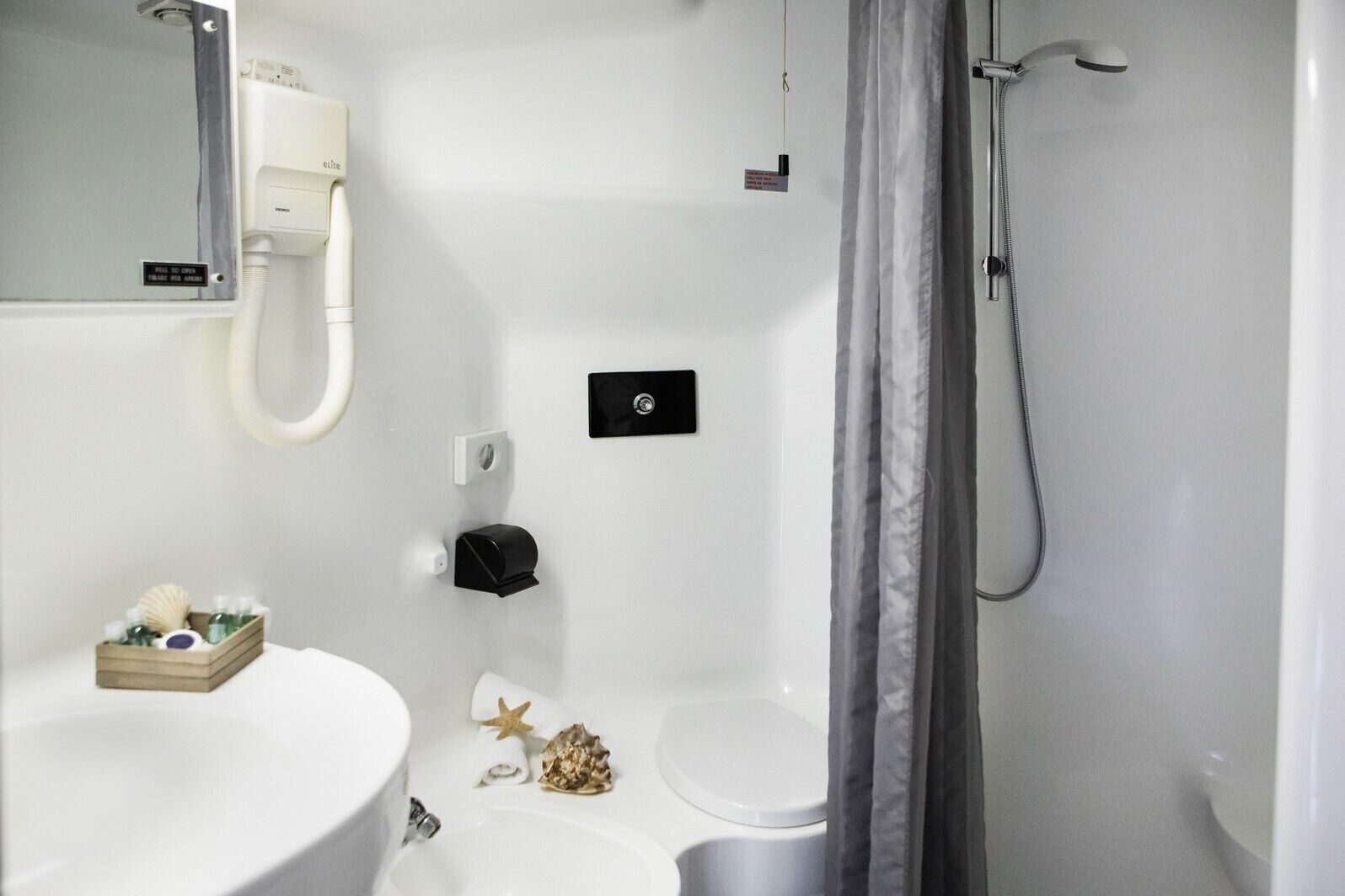 Un baño con lavamanos, inodoro y ducha blancos. Hay un perchero con un adorno de estrella y una pequeña caja de madera con artículos de aseo.
