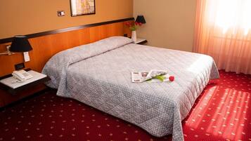 A hotel room with a bed, a nightstand, a lamp, a telephone, and a vase with flowers.