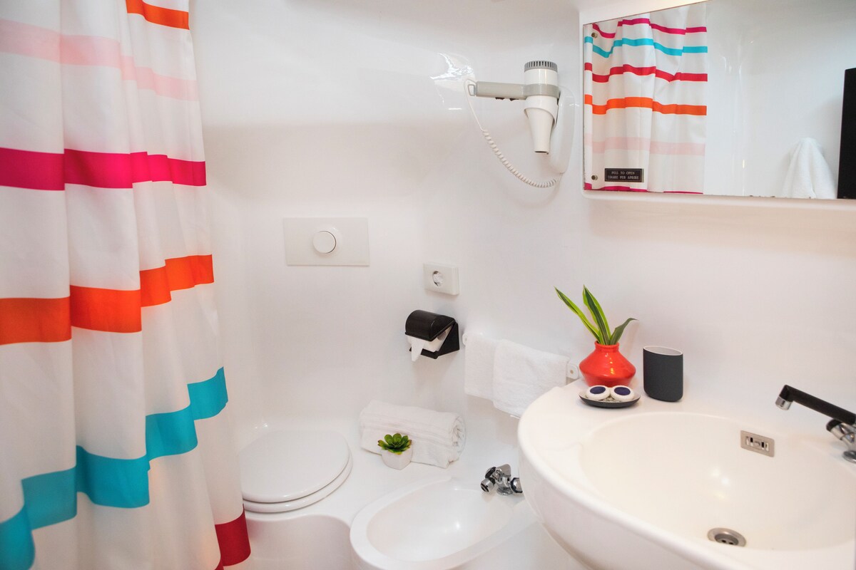 A bathroom with a toilet, bidet, sink, and a hairdryer mounted on the wall.