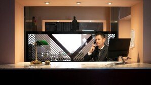 A reception desk with a modern design, featuring a glass partition and a patterned backdrop. - Hotel Milano Pool & Garden (Godiasco)