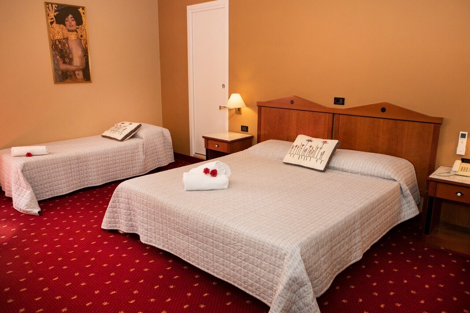 A hotel room with two beds, a wooden headboard, a bedside table with a lamp, and a telephone.