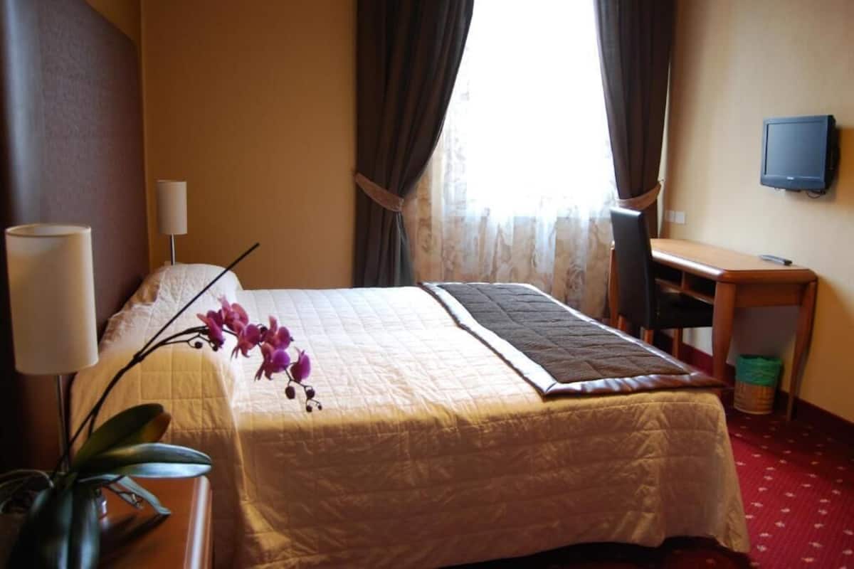 A hotel room with a bed, a desk, a television, and a window with curtains.
