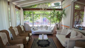 A spacious living area with a white sofa, two wicker chairs, a coffee table, and a large window with a view of greenery outside. - Hotel Milano Pool & Garden (Godiasco)