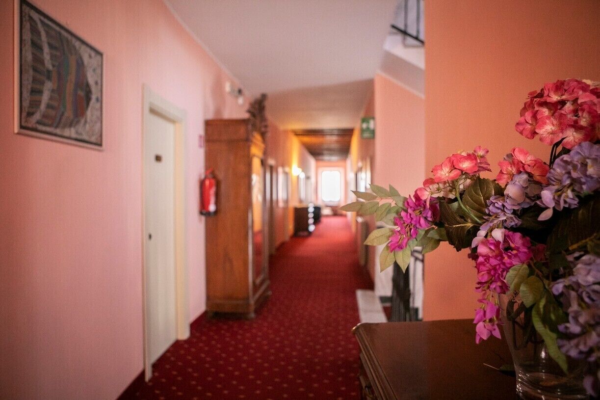 Ein Hotelgang mit rotem Teppich, einer Holztür und einem Blumenstrauß auf einem Tisch.
