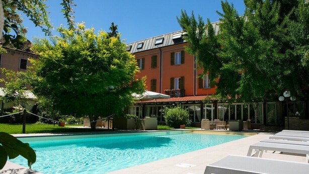 A swimming pool with lounge chairs, surrounded by trees and a building with multiple windows. - Hotel Milano Pool & Garden (Godiasco)