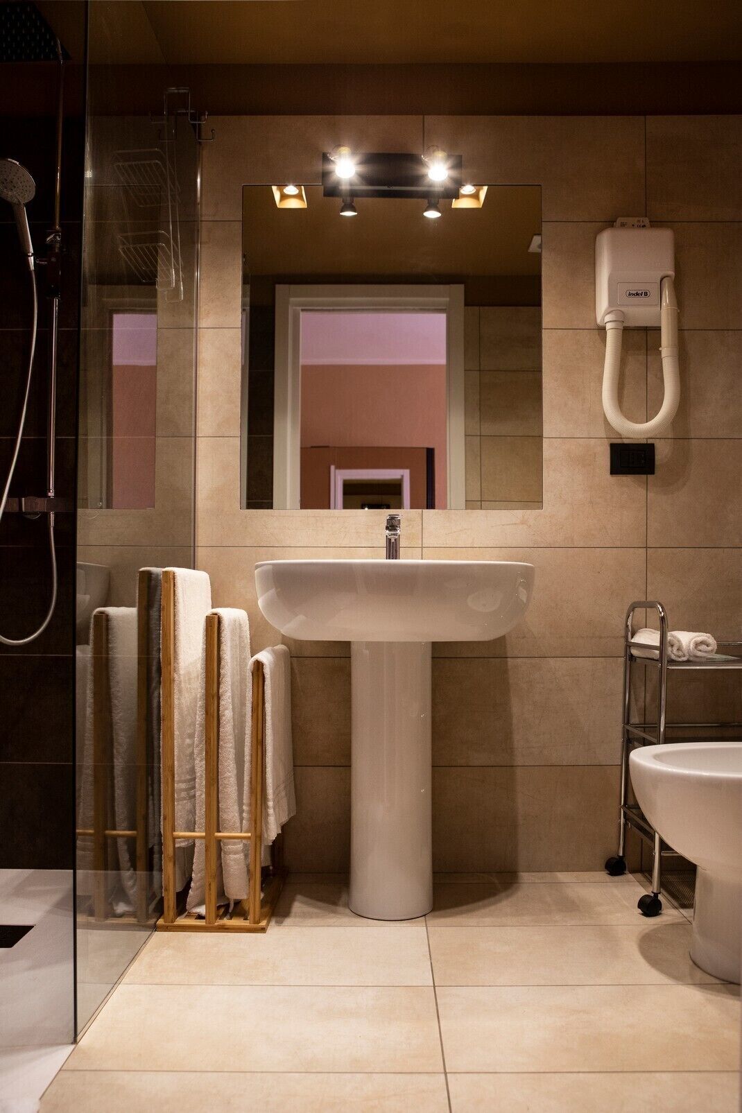 Een moderne badkamer met een wastafel op voetstuk, een glazen douchecabine en een handdoekrek.