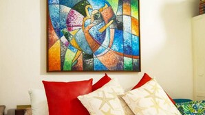 A bed with white bedding, red and beige pillows, and a colorful abstract painting above it. - Entire rented housing in Cartagena de Indias, Colombia (Cartagena de Indias)