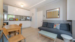 Una cocina moderna con armarios blancos, una mesa de comedor con sillas, un sofá gris con cojines y una pequeña mesa blanca.