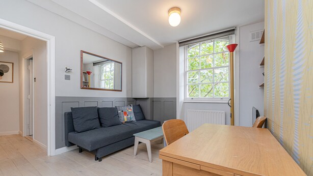 Una sala de estar moderna con un sofá gris, una mesa de comedor de madera y un ventanal con vistas a árboles.