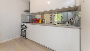 Una cocina moderna con armarios blancos, horno empotrado y microondas rojo.