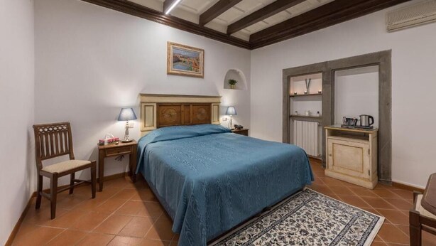 Un dormitorio con una cama, una silla, un escritorio, una lámpara, un estante y un espejo.