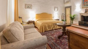 Un dormitorio con cama, sofá, una mesita, un radiador y un cuadro en la pared.