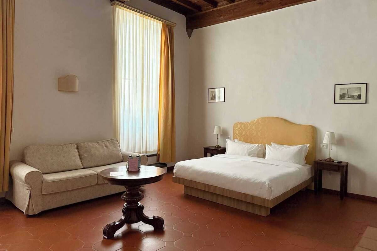 Une chambre d’hôtel avec un lit, un canapé, une table ronde et une fenêtre avec des rideaux.