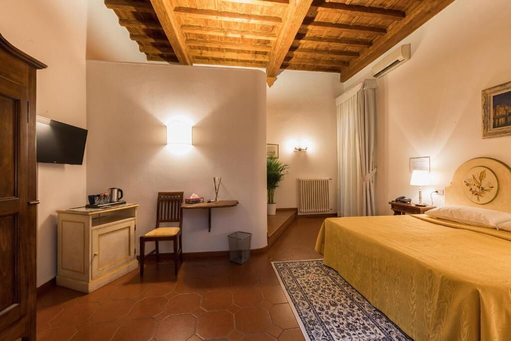 Une chambre confortable avec un plafond en bois, un lit recouvert d’une couverture jaune, un petit bureau avec une chaise, un radiateur et un téléviseur fixé au mur.