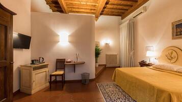Une chambre confortable avec un plafond en bois, un lit recouvert d’une couverture jaune, un petit bureau avec une chaise, un radiateur et un téléviseur fixé au mur.