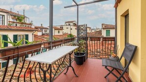 Un balcón con mesa y sillas, plantas en macetas y vistas a edificios cercanos.