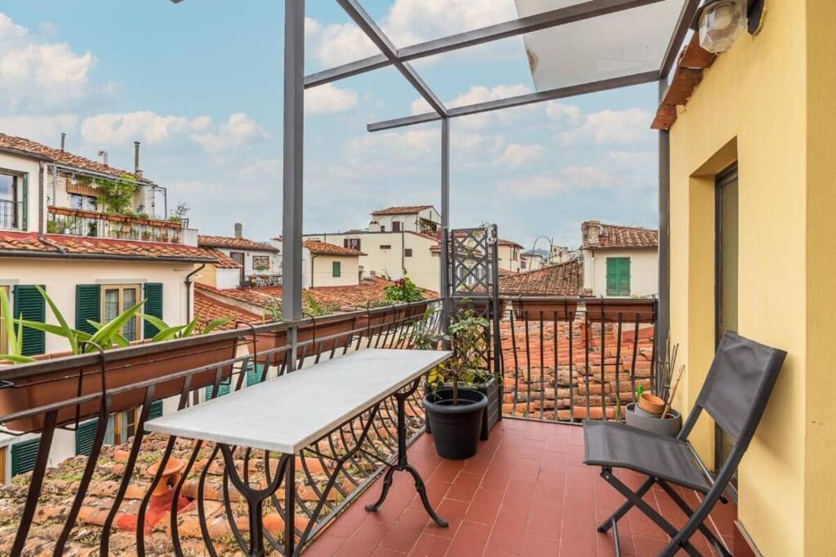 Un balcon avec une table et des chaises, des plantes en pot et une vue sur les bâtiments voisins.